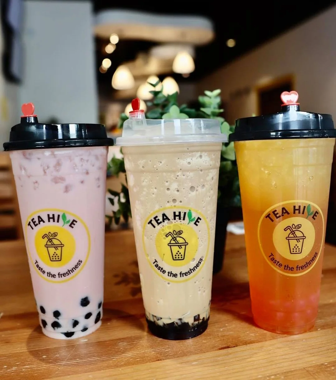 Three colorful drinks with various toppings served in clear cups, featuring a logo and small decorative lids.