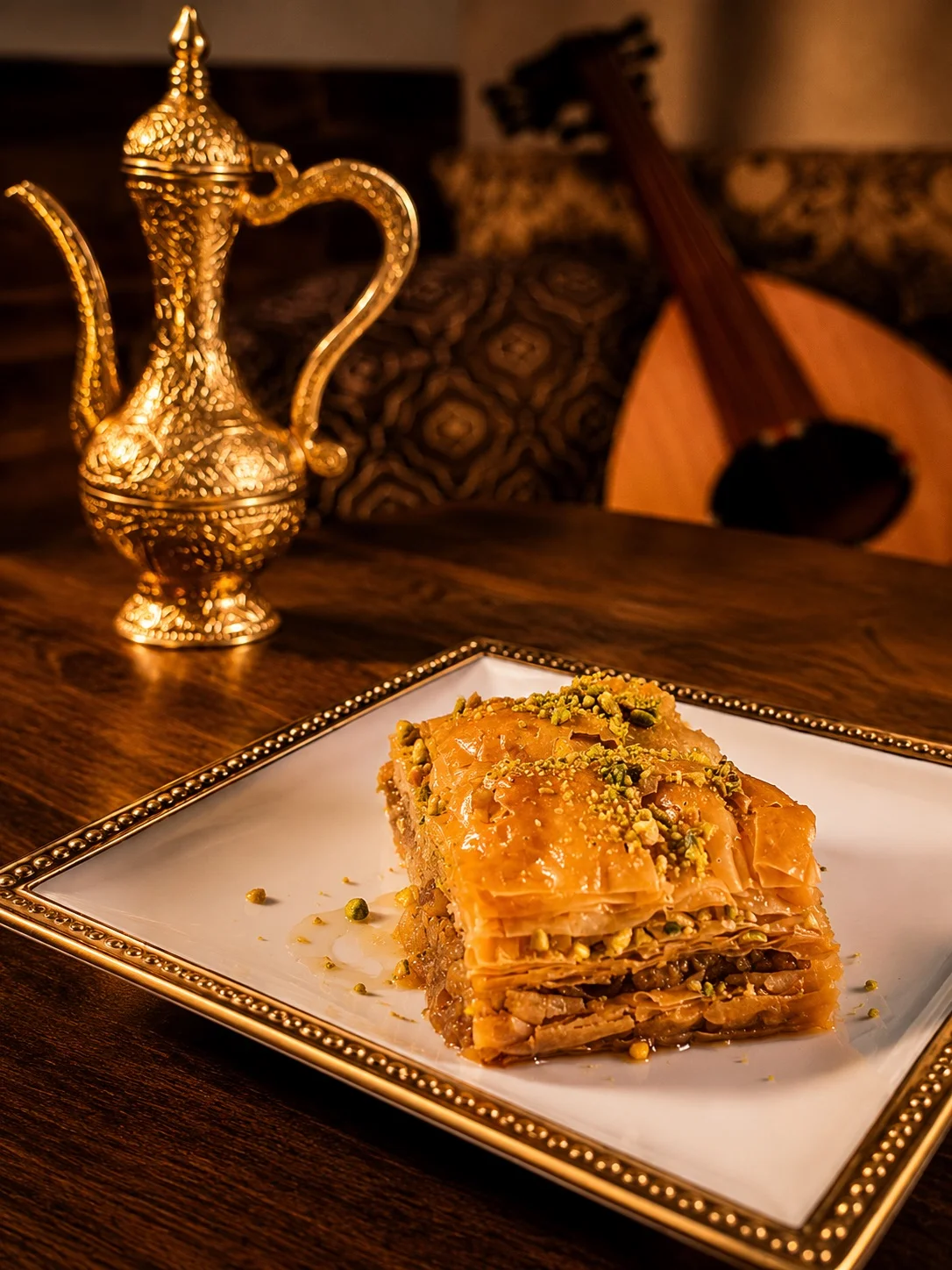 A plate of baklava topped with pistachios and a decorative coffee pot in the background.