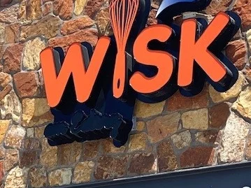 Restaurant sign for WISK with a whisk logo on a stone wall