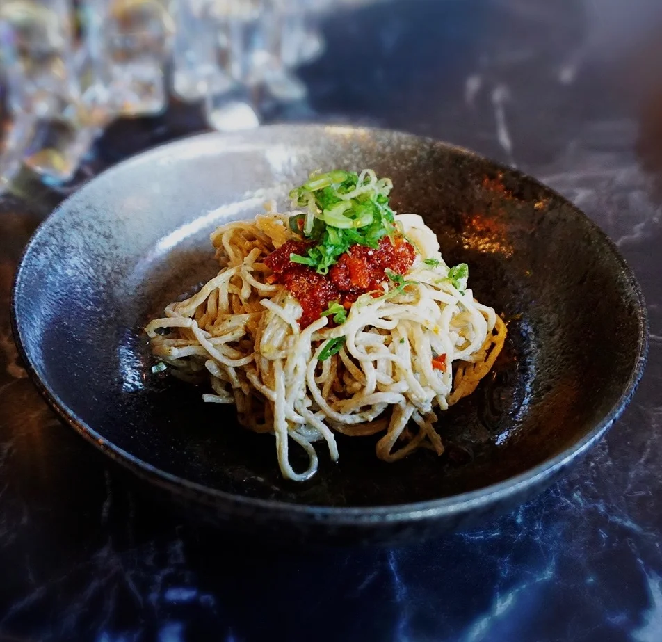 Plate of noodles topped with green onions and red sauce.