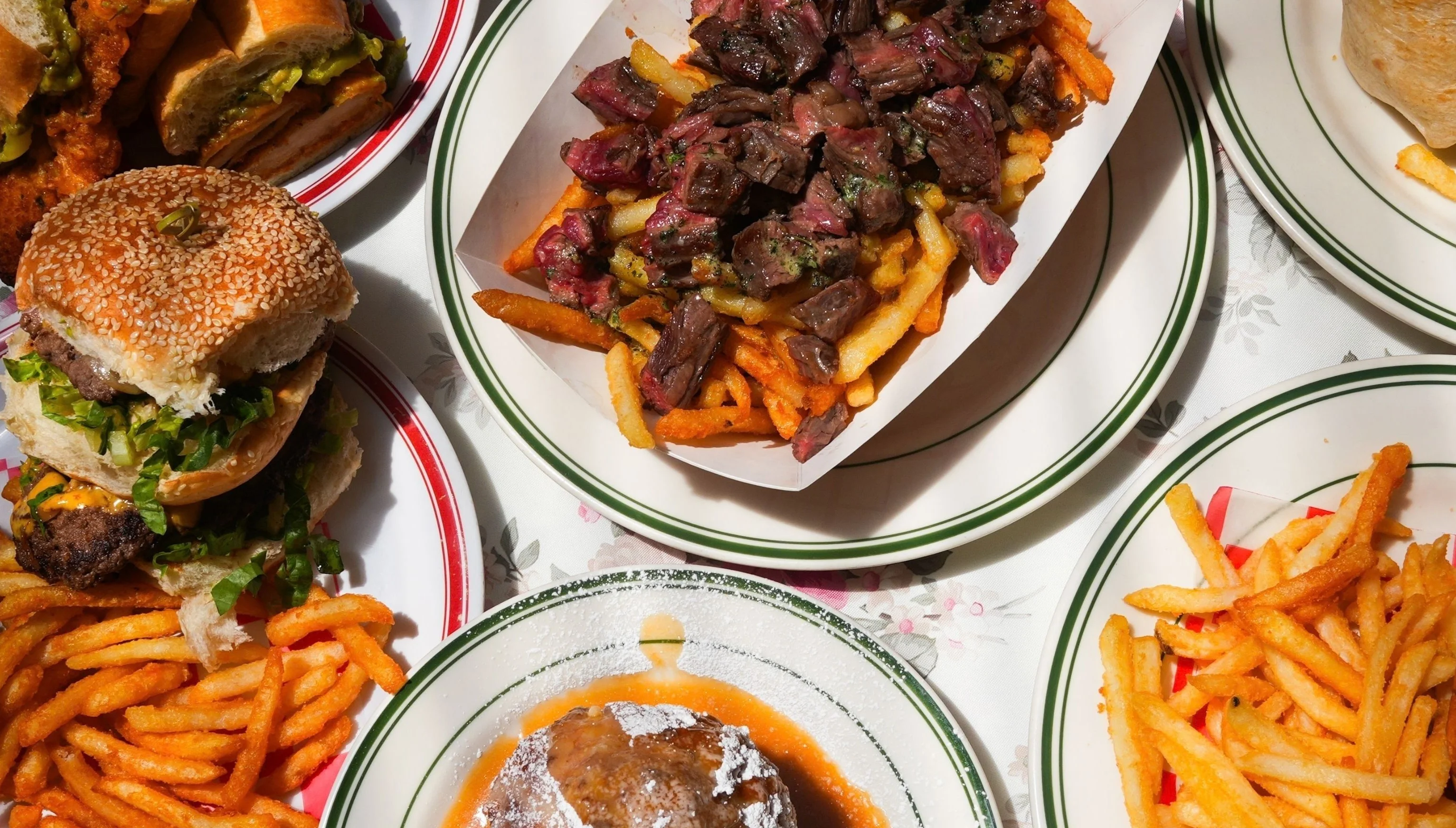 Overhead table spread at Uncle Rocco in Hoboken - burgers, sandwiches, a wrap, steak over fries and sides of fries