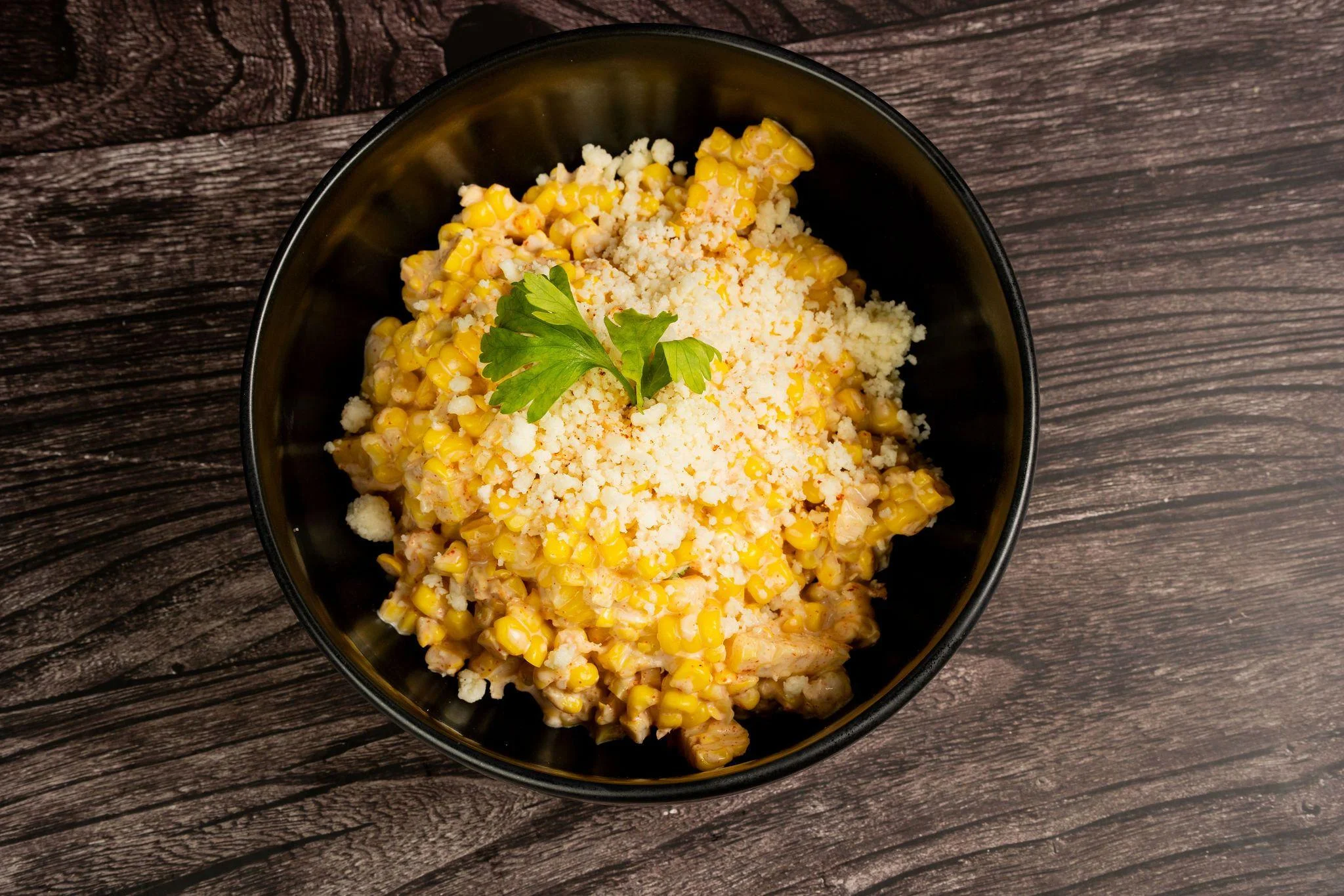 A bowl of creamy corn with cheese and a garnish of fresh herbs.