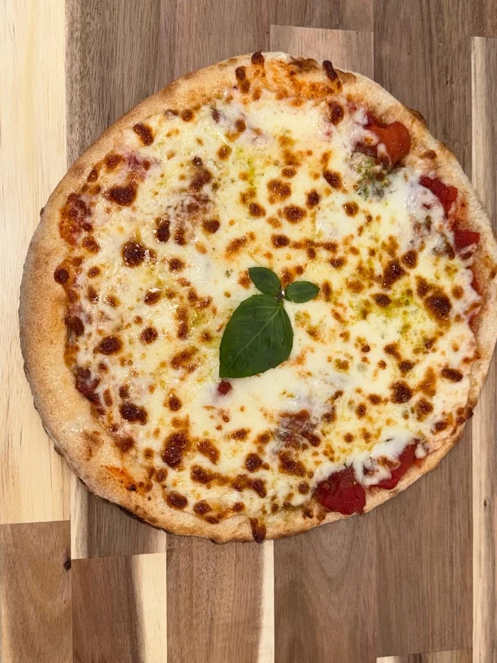 A classic Margherita pizza with a golden crust, topped with melted cheese, tomato sauce, and a fresh basil leaf.