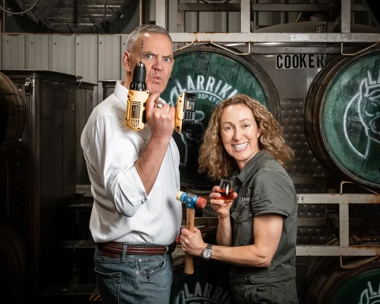 Two people posing with tools and drinks in a brewery setting