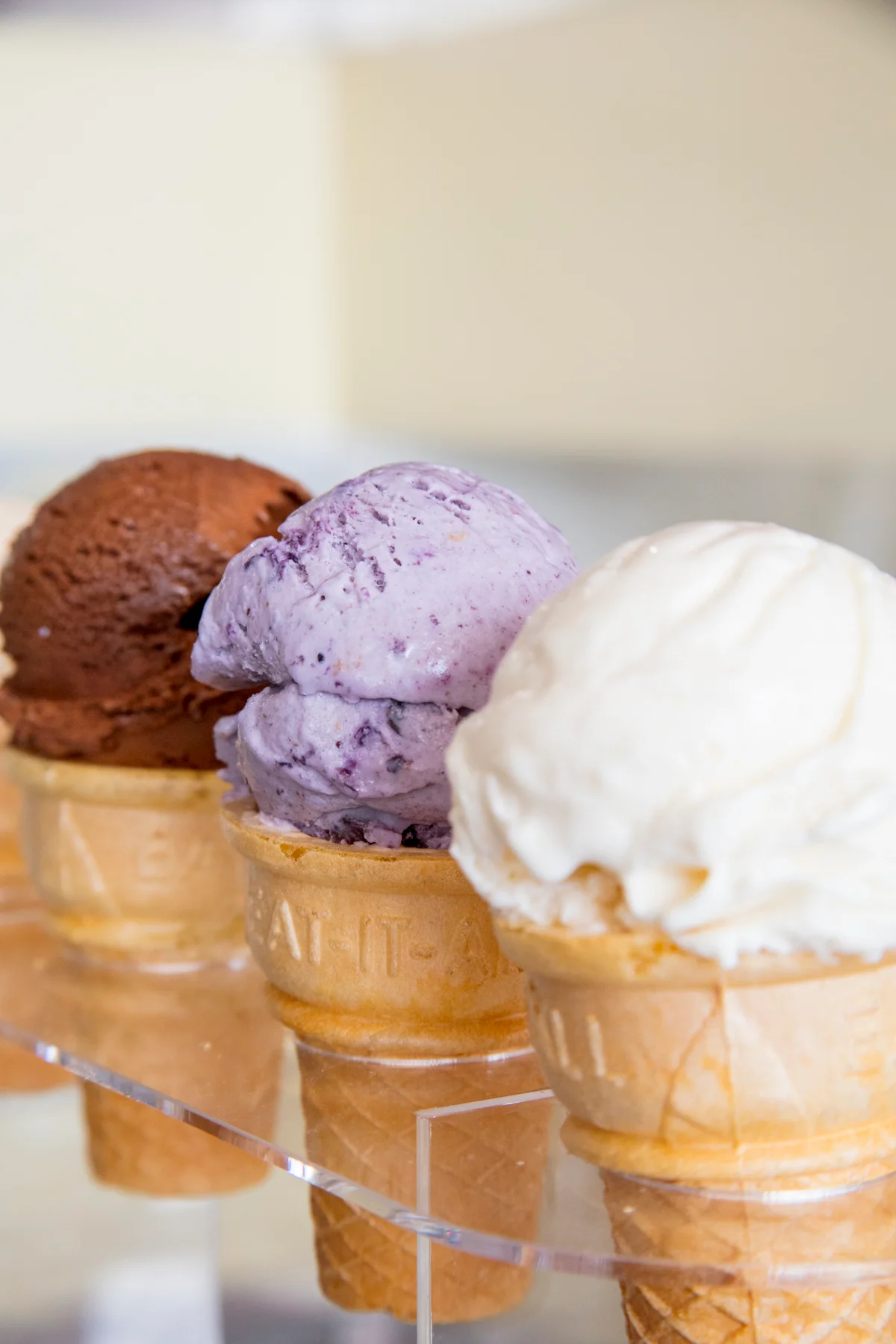 Three ice cream cones lined up on display, featuring scoops of chocolate, blueberry, and vanilla chef-inspired ice cream from Hugs, a Northwest Arkansas scoop shop