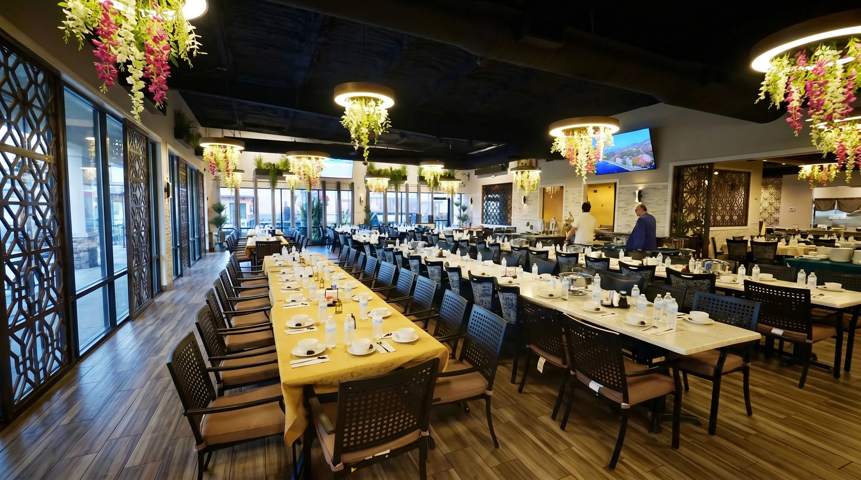 An elegantly arranged dining area with a long table set for a large group, featuring decorative hanging plants and ambient lighting.