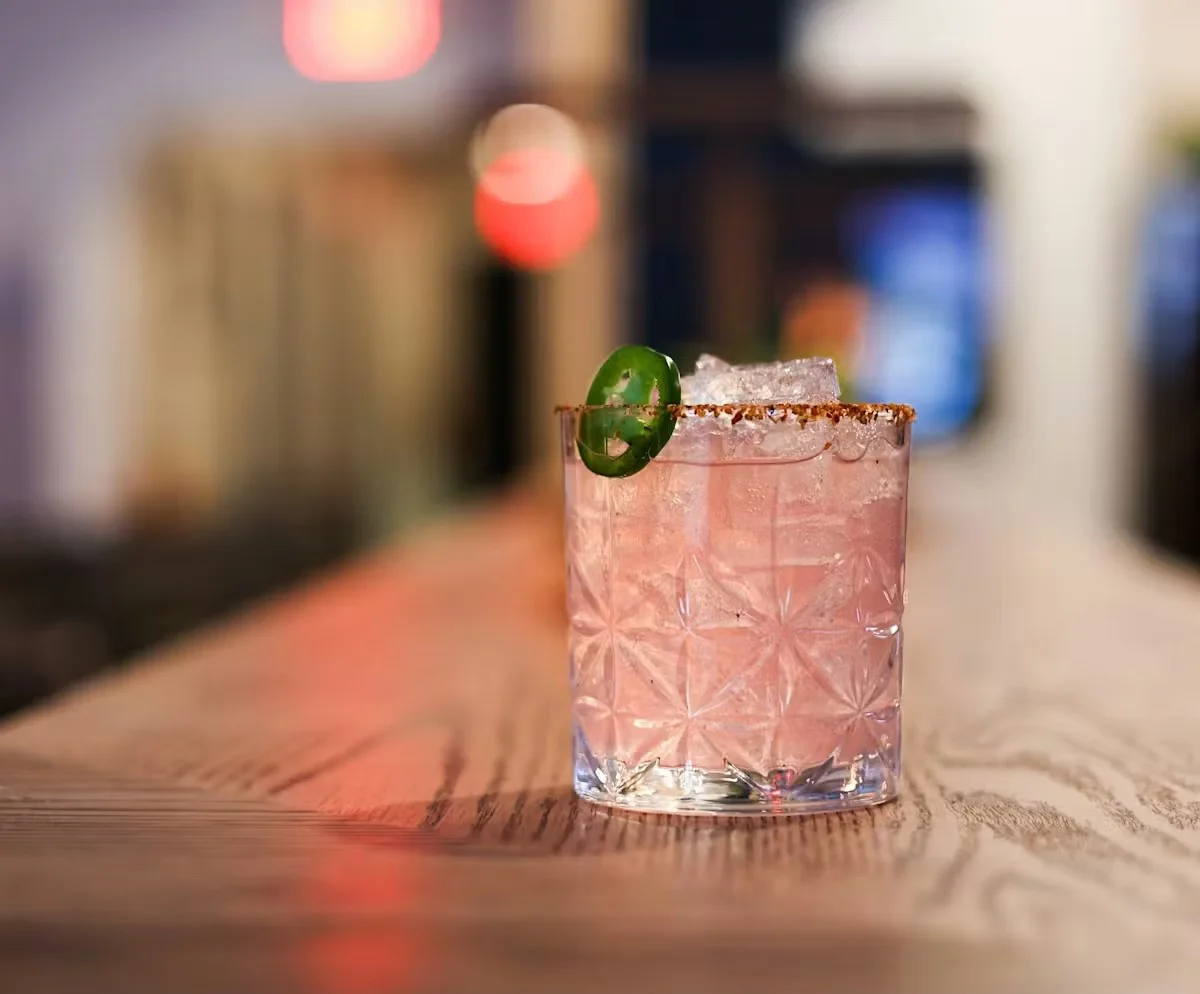 A vibrant cocktail with ice and an orange twist on a marble table.