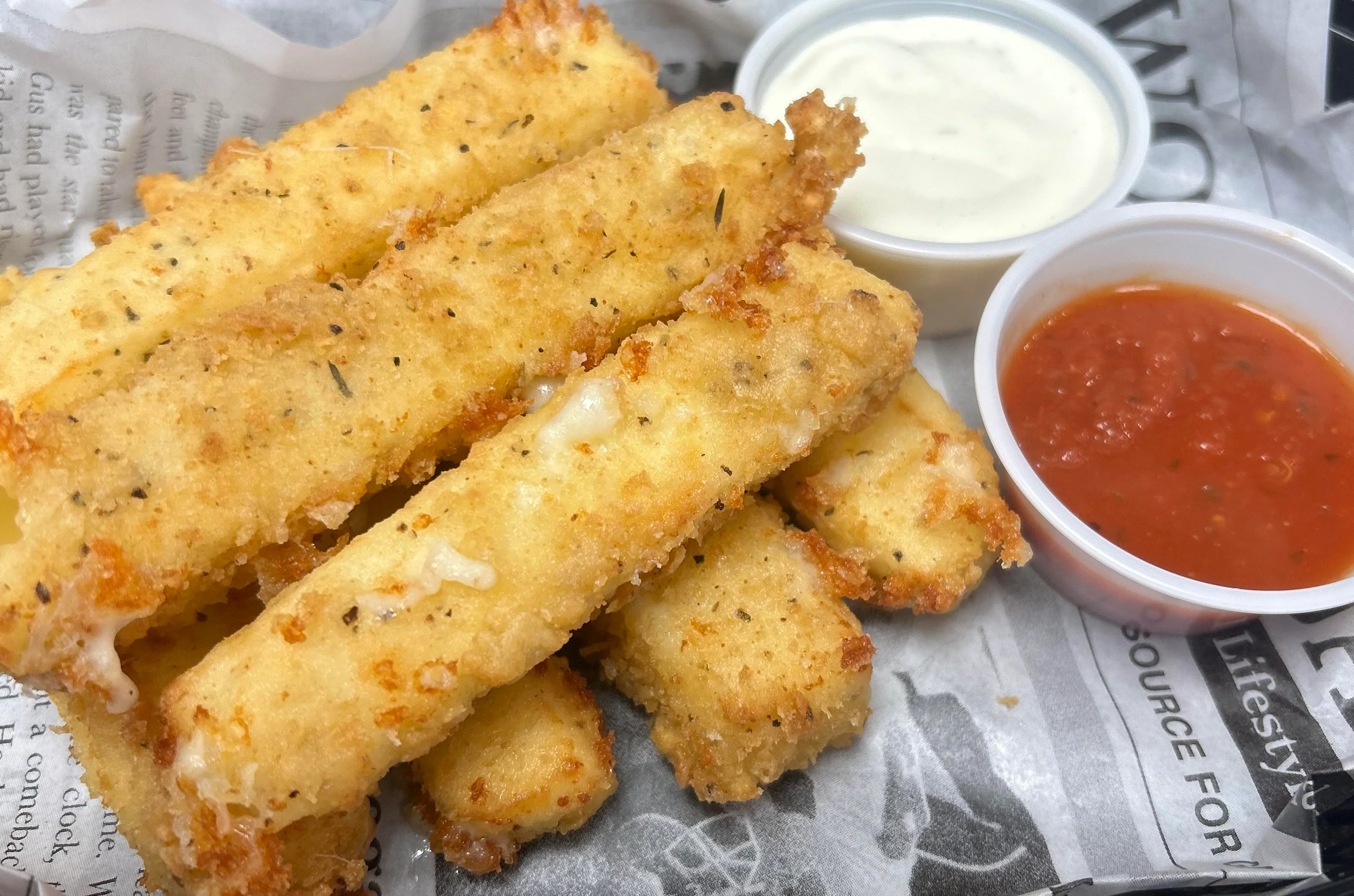 A plate of fried cheese sticks served with marinara sauce and ranch dressing.