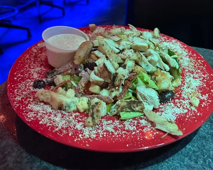 A colorful plate of salad topped with grilled chicken, cheese, and a side of dressing.