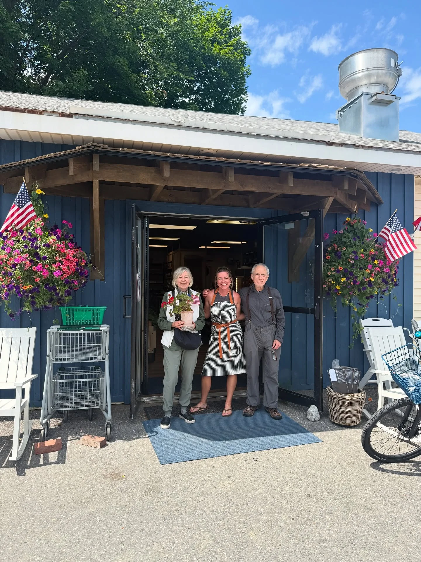 Friendly staff outside a charming restaurant with flowers and American flags