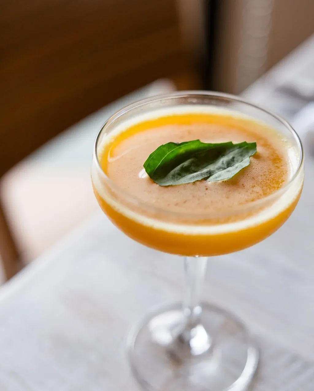 Craft cocktail with orange hue and basil garnish