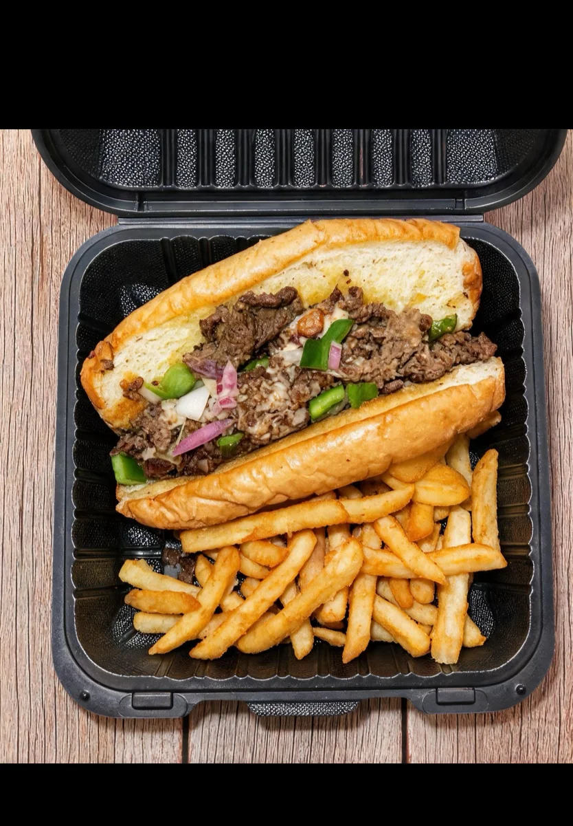 Philly cheesesteak sandwich with fries in a takeout container