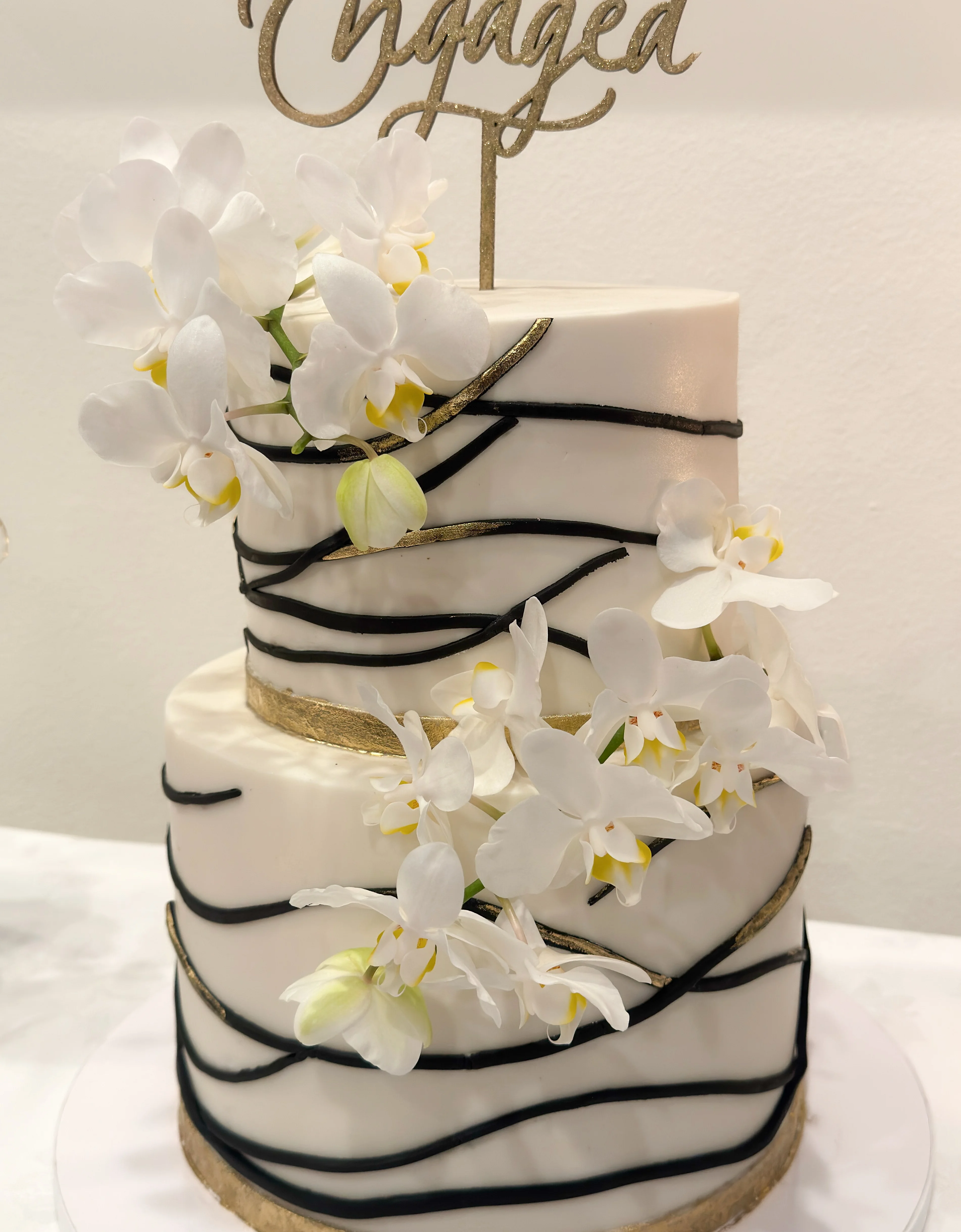 Elegant two-tier wedding cake with orchids and 'Engaged' topper.