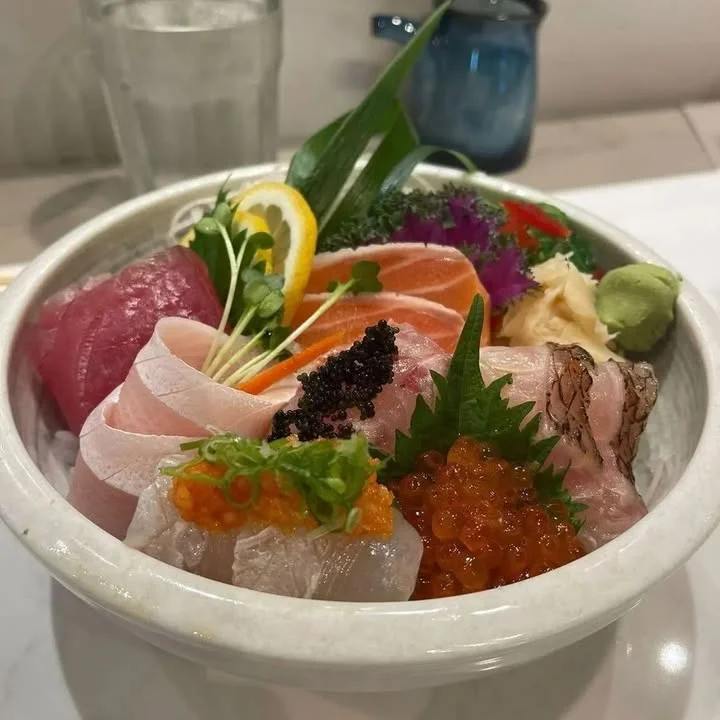 A vibrant bowl of assorted sashimi, featuring various types of fresh fish, garnished with colorful vegetables and herbs.
