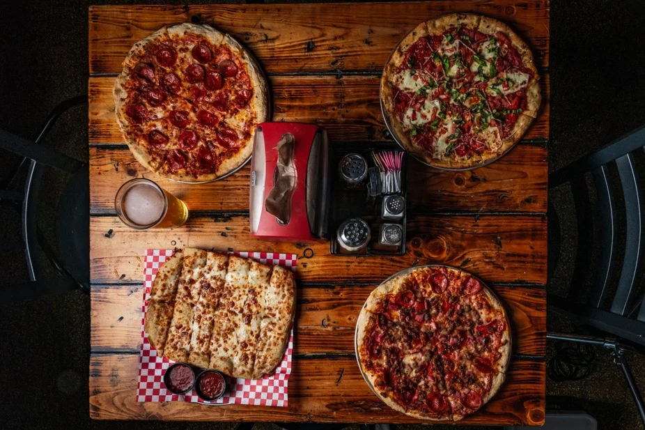A round pizza topped with red sauce, mozzarella cheese, and fresh basil leaves placed on a wooden table.