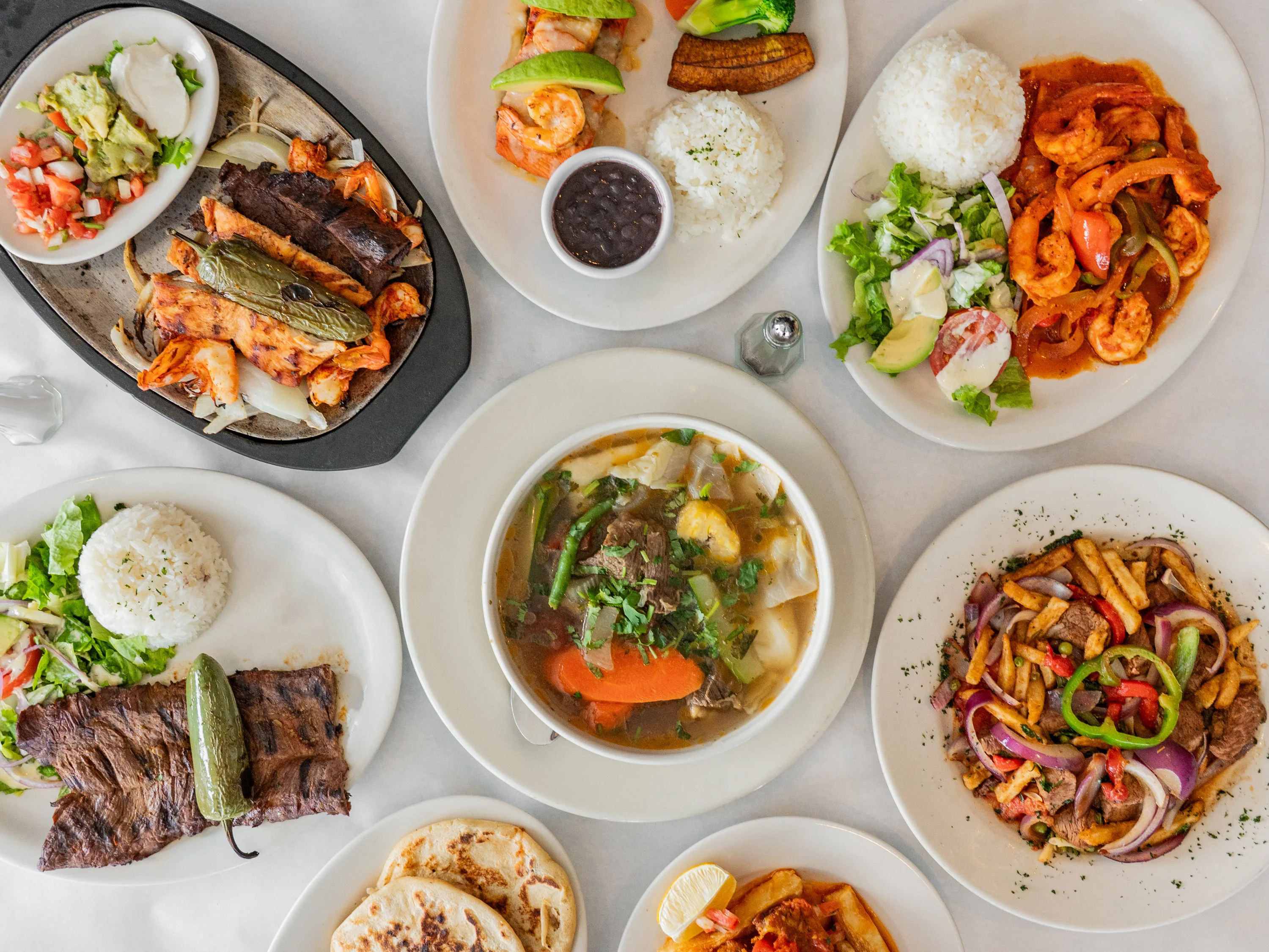 An assortment of dishes featuring grilled meats, shrimp, rice, vegetables, and sides, beautifully arranged on a table.
