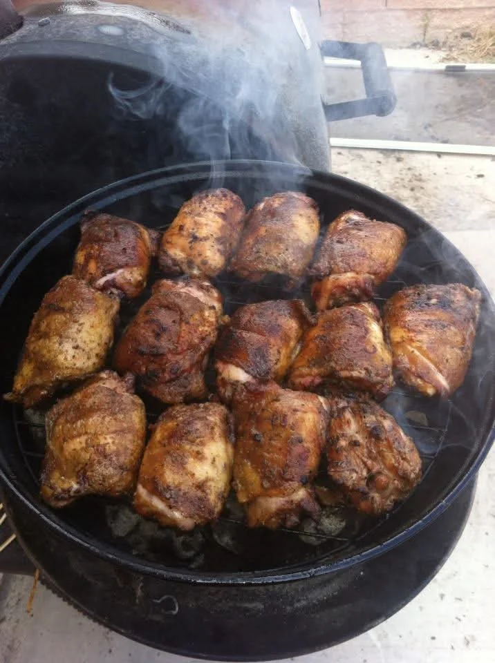 A grill filled with multiple pieces of chicken, emitting smoke as they cook.