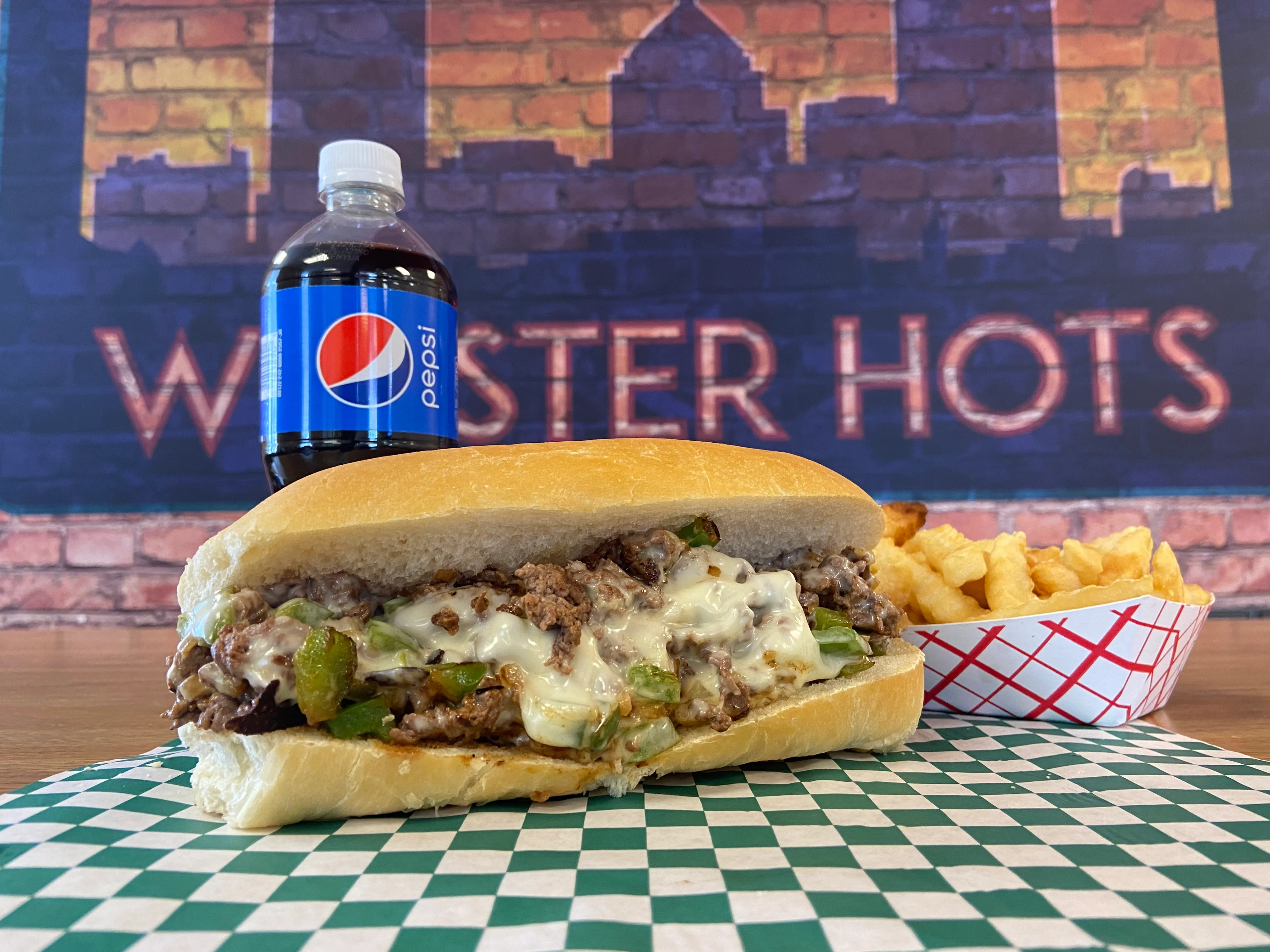 Philly cheesesteak sandwich with fries and a soda