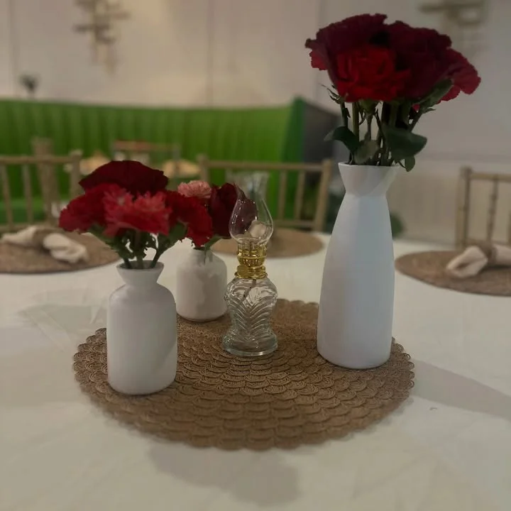 A charming table centerpiece featuring white and red flowers in decorative vases and a vintage lantern, set on a circular mat.