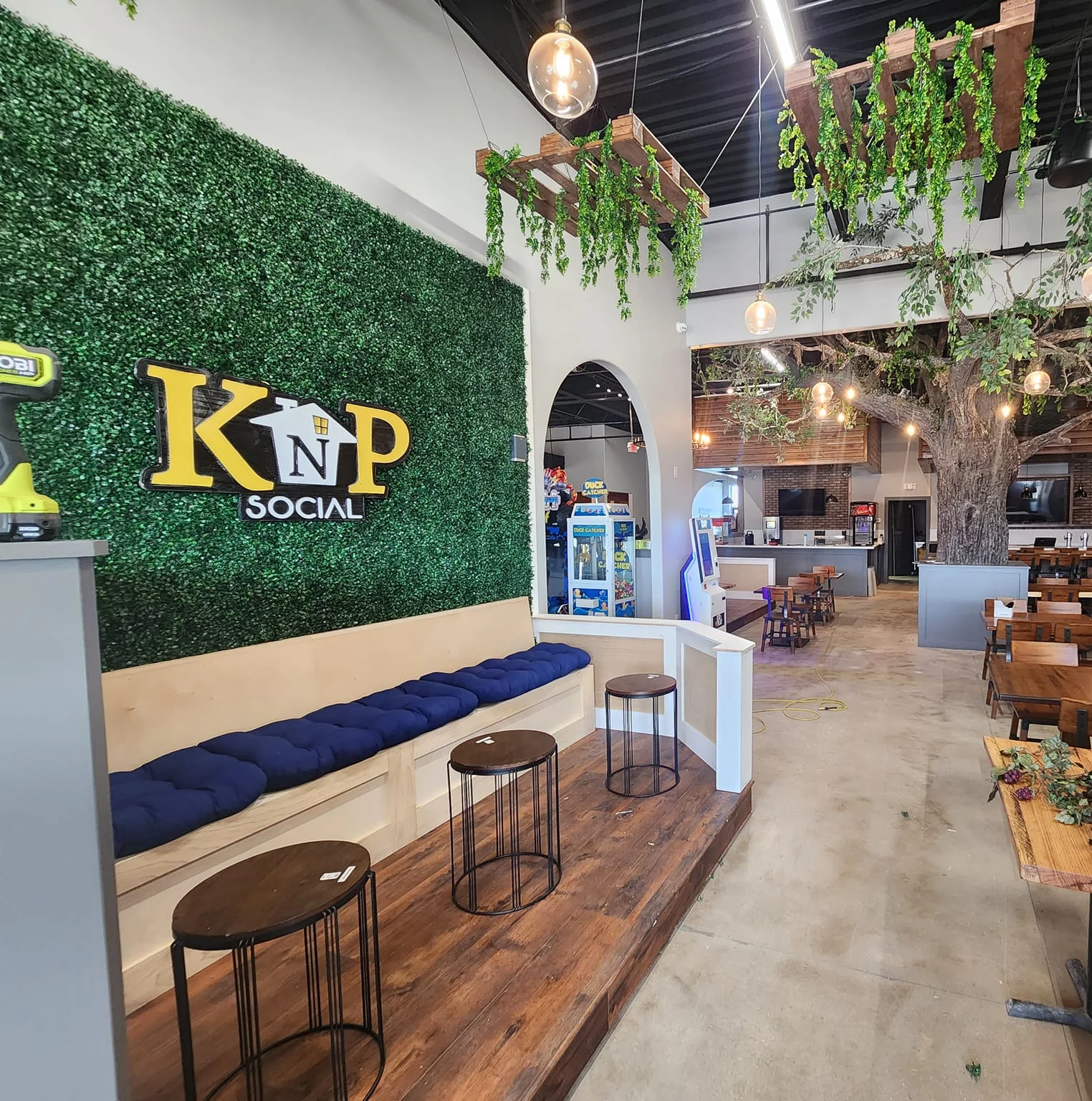 Interior of KNP Social with seating, greenery, and a large tree.