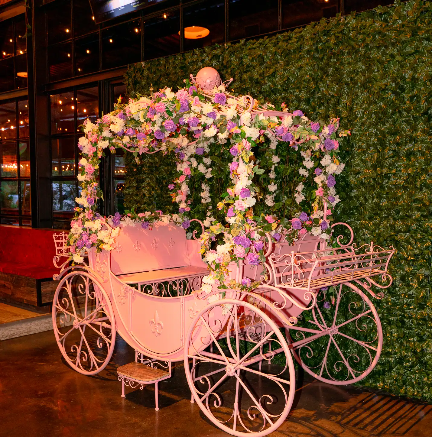 Pink flower-covered carriage photo op inside Pour Behavior Houston, styled with floral decor and green hedge backdrop for private parties and Instagram moments.