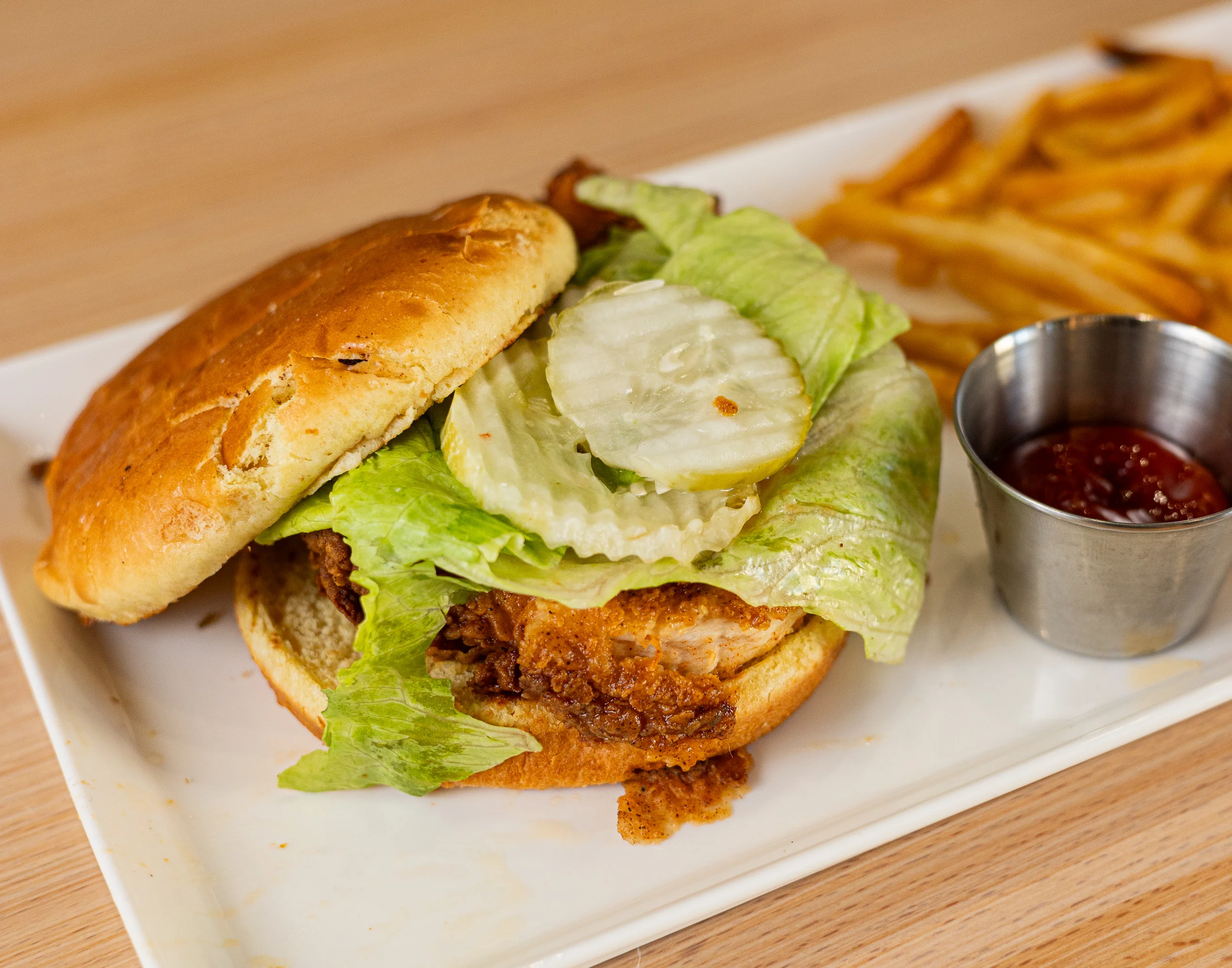 Fried chicken sandwich with lettuce, pickles, and fries on a plate.