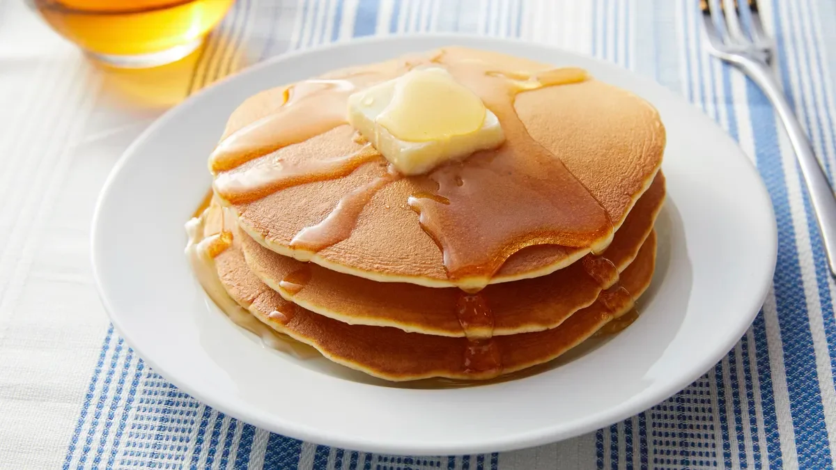 A stack of fluffy pancakes topped with butter and drizzled with syrup, served on a white plate.