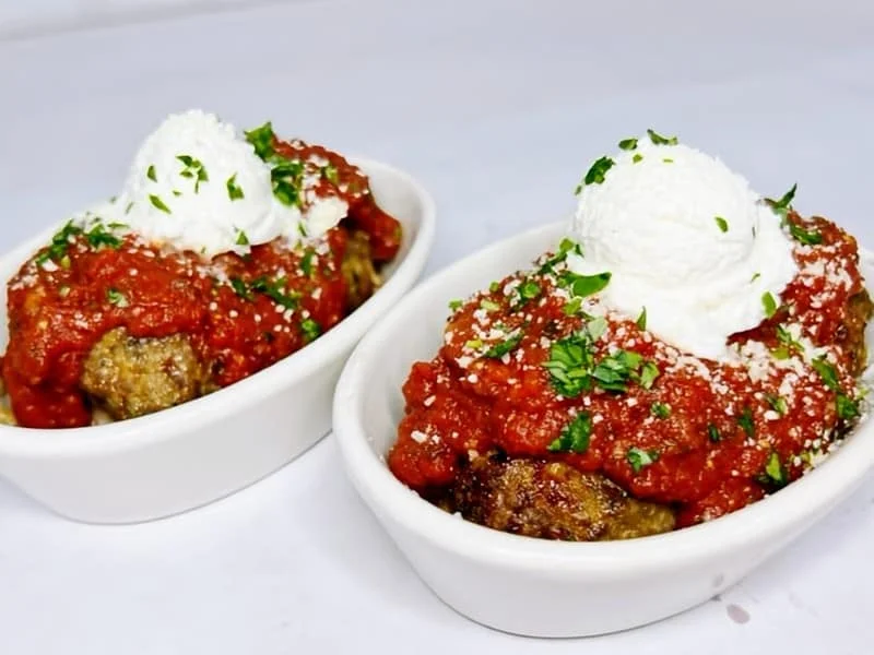 Two bowls of meatballs topped with marinara sauce, herbs, and a dollop of creamy cheese.