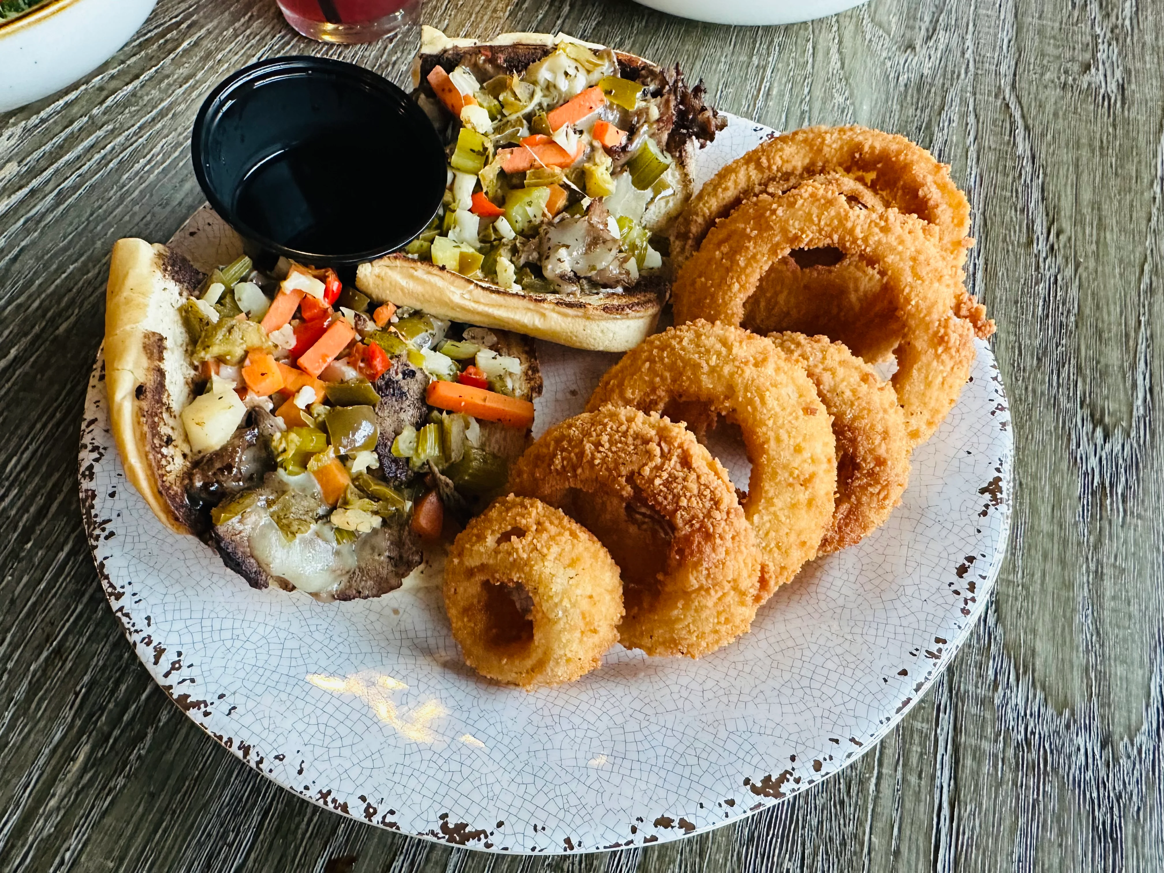 A serving plate featuring two sandwiches topped with diced vegetables, alongside a portion of crispy onion rings.
