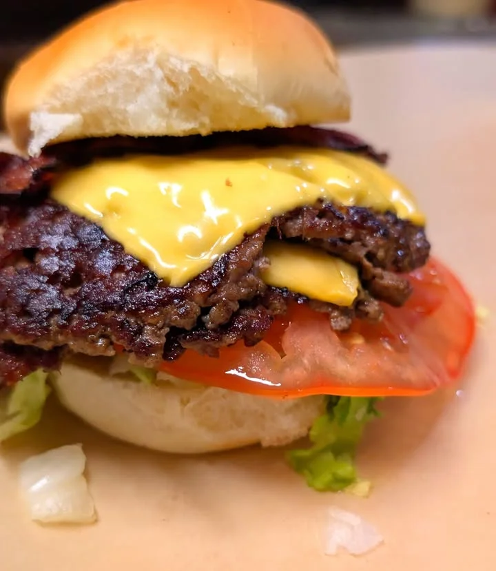 A close-up of a delicious cheeseburger with two layers of melted cheese, tomato, and lettuce on a soft bun.