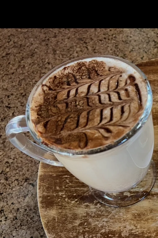 A creamy beverage with a decorative cocoa powder design on top, served in a transparent mug.