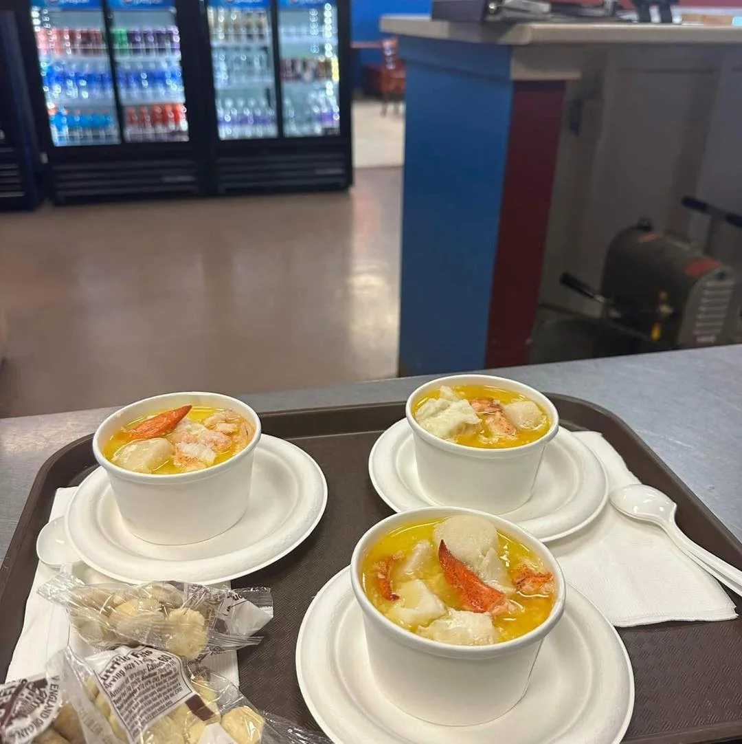 Three cups of seafood stew containing shrimp and fish in a yellow broth, served on a tray with some crackers.