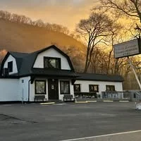 A modern building with a sloped roof, surrounded by trees. The sky is painted with hues of orange and yellow, indicating sunset.