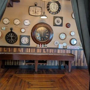 Wall adorned with various clocks and a wooden table in a cozy setting.
