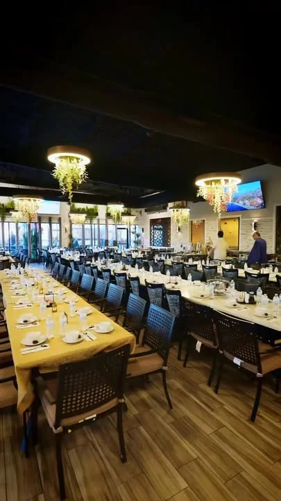 An elegantly arranged dining area with a long table set for a large group, featuring decorative hanging plants and ambient lighting.