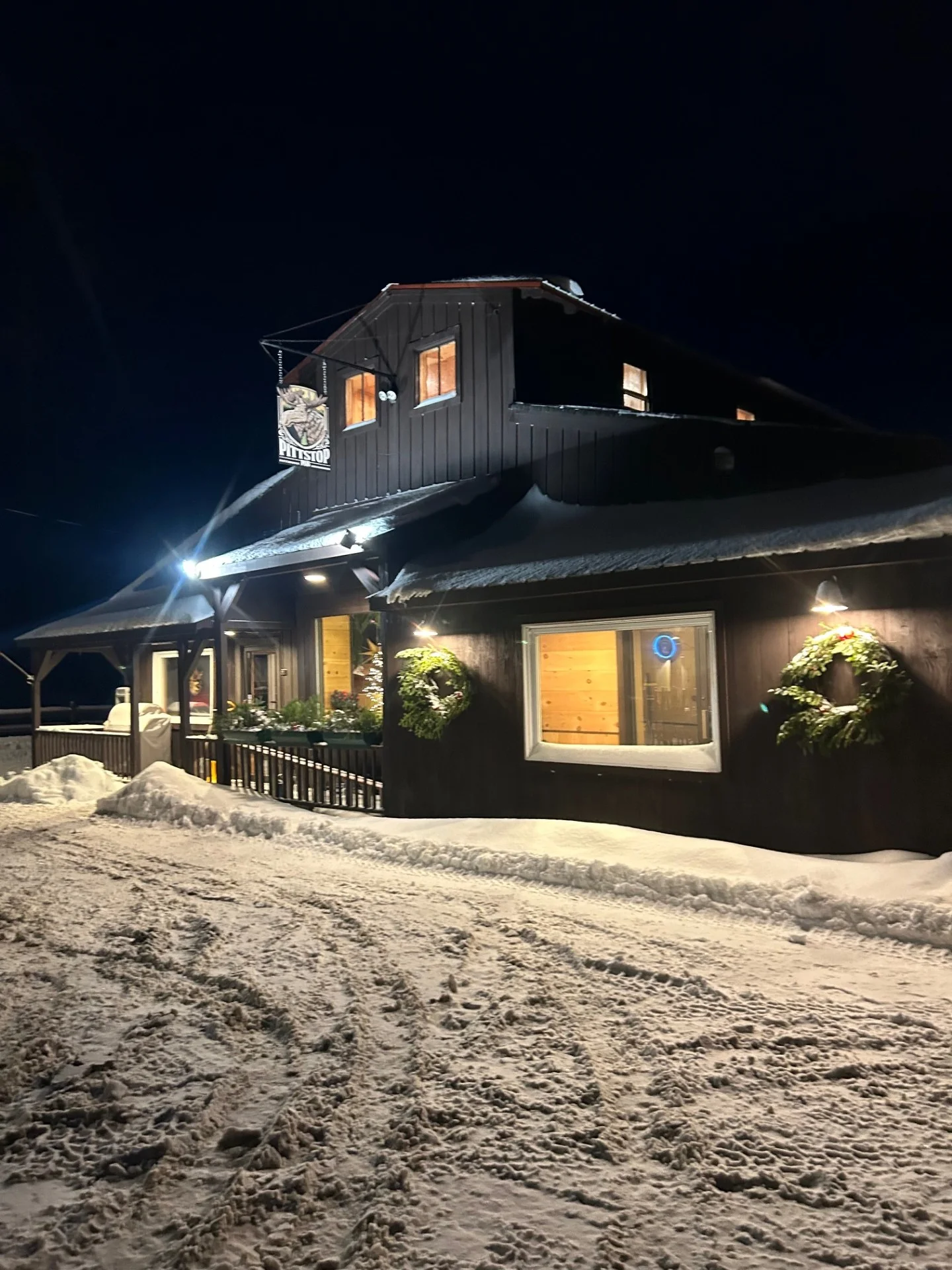 A cozy pub exterior illuminated at night, surrounded by snow. The building features a sign and an American flag.