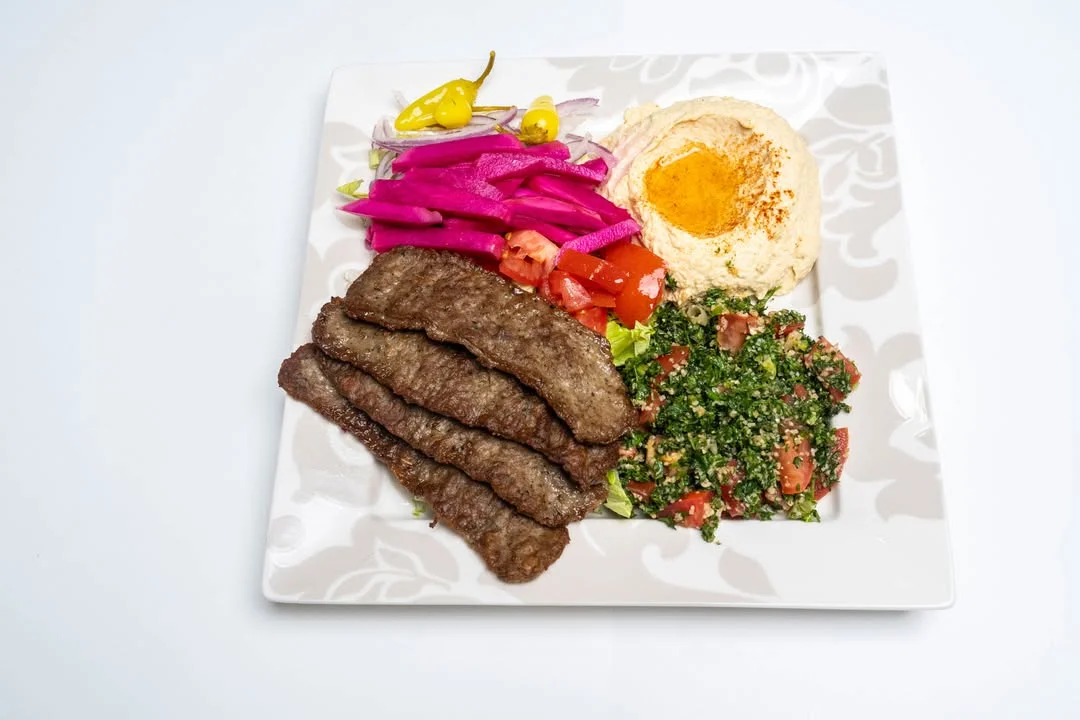 A plate featuring grilled meat strips alongside hummus, salad, and pickled vegetables.