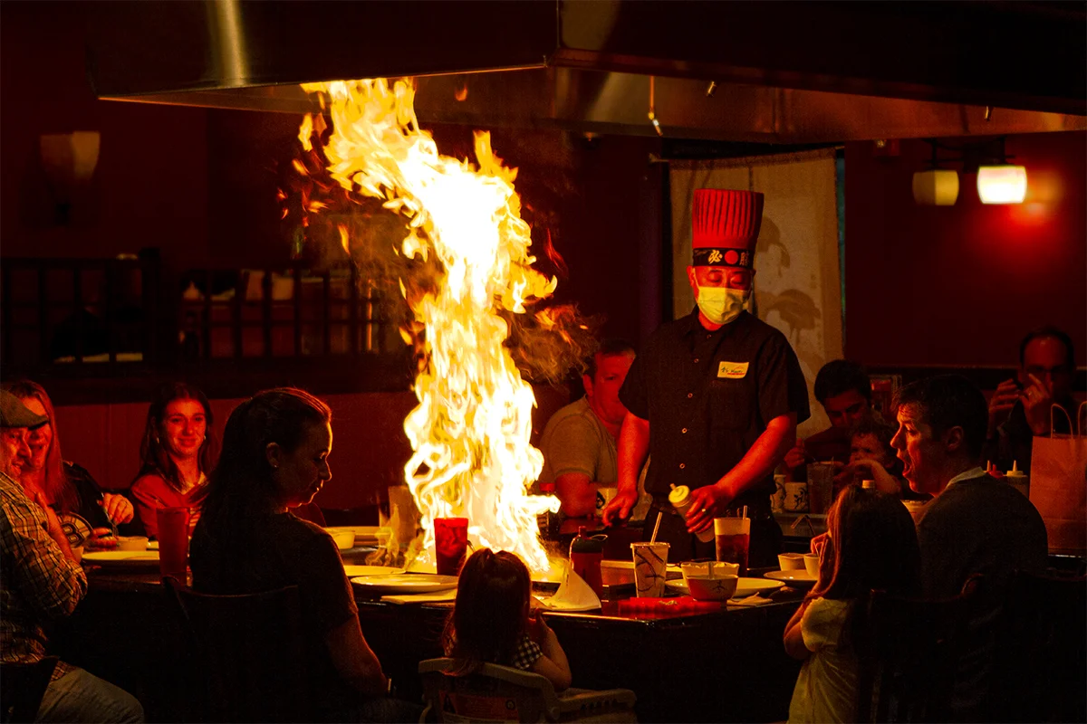 Hibachi chef performing with flames while guests watch at a teppanyaki table at Mahzu in East Windsor, NJ
