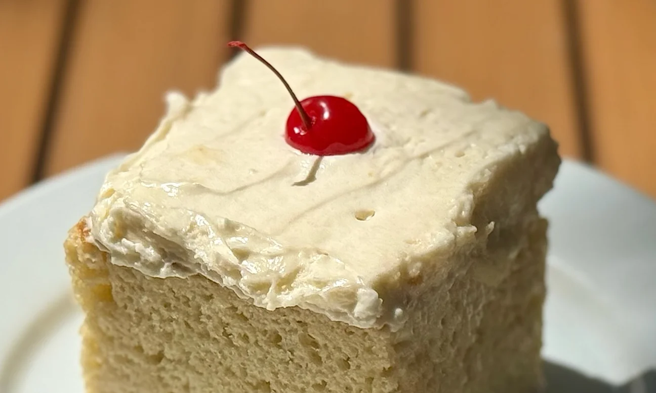 Slice of classic vanilla cake with buttercream frosting and cherry on top