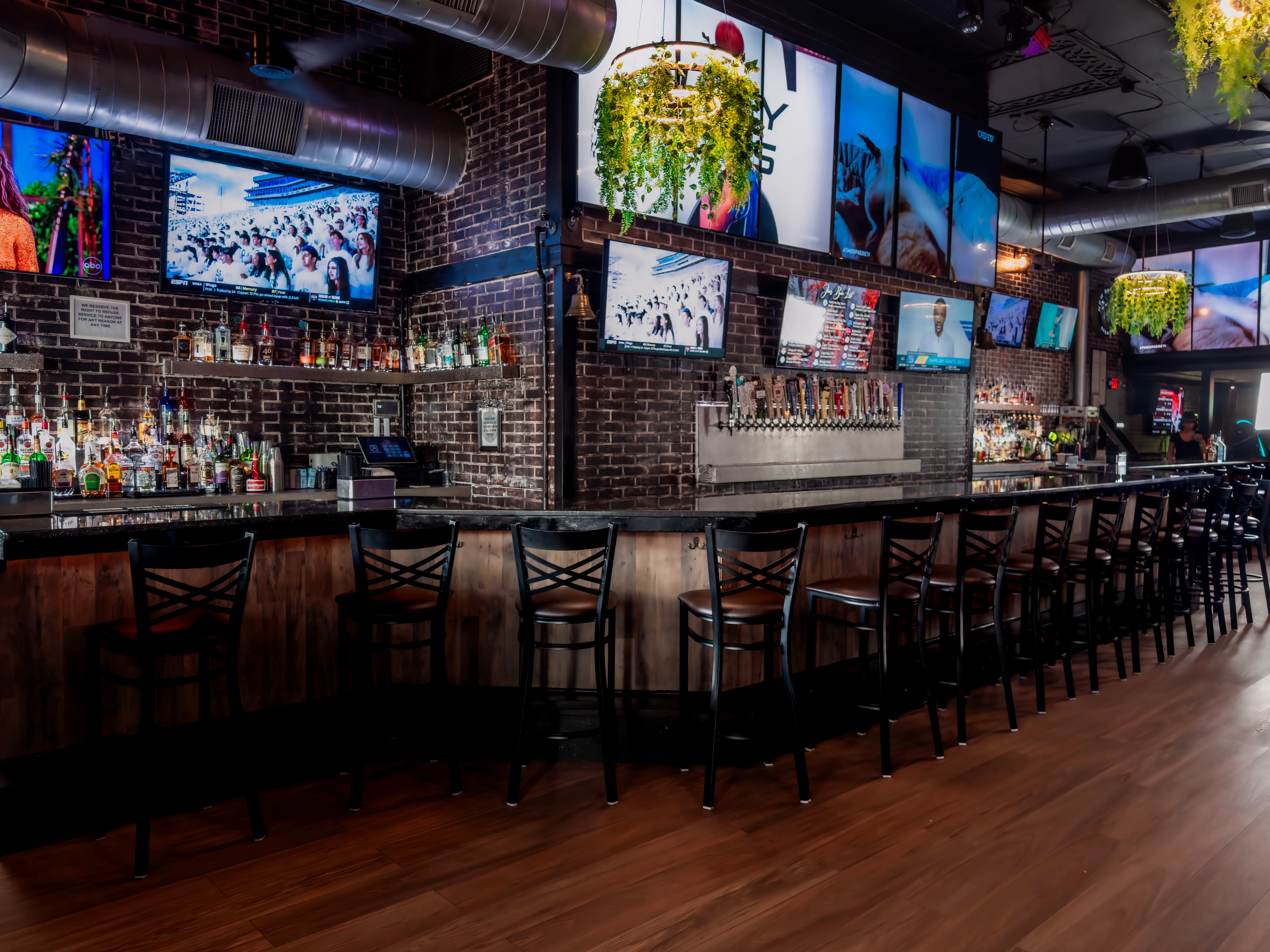 Modern bar interior with exposed brick and multiple screens displaying sports