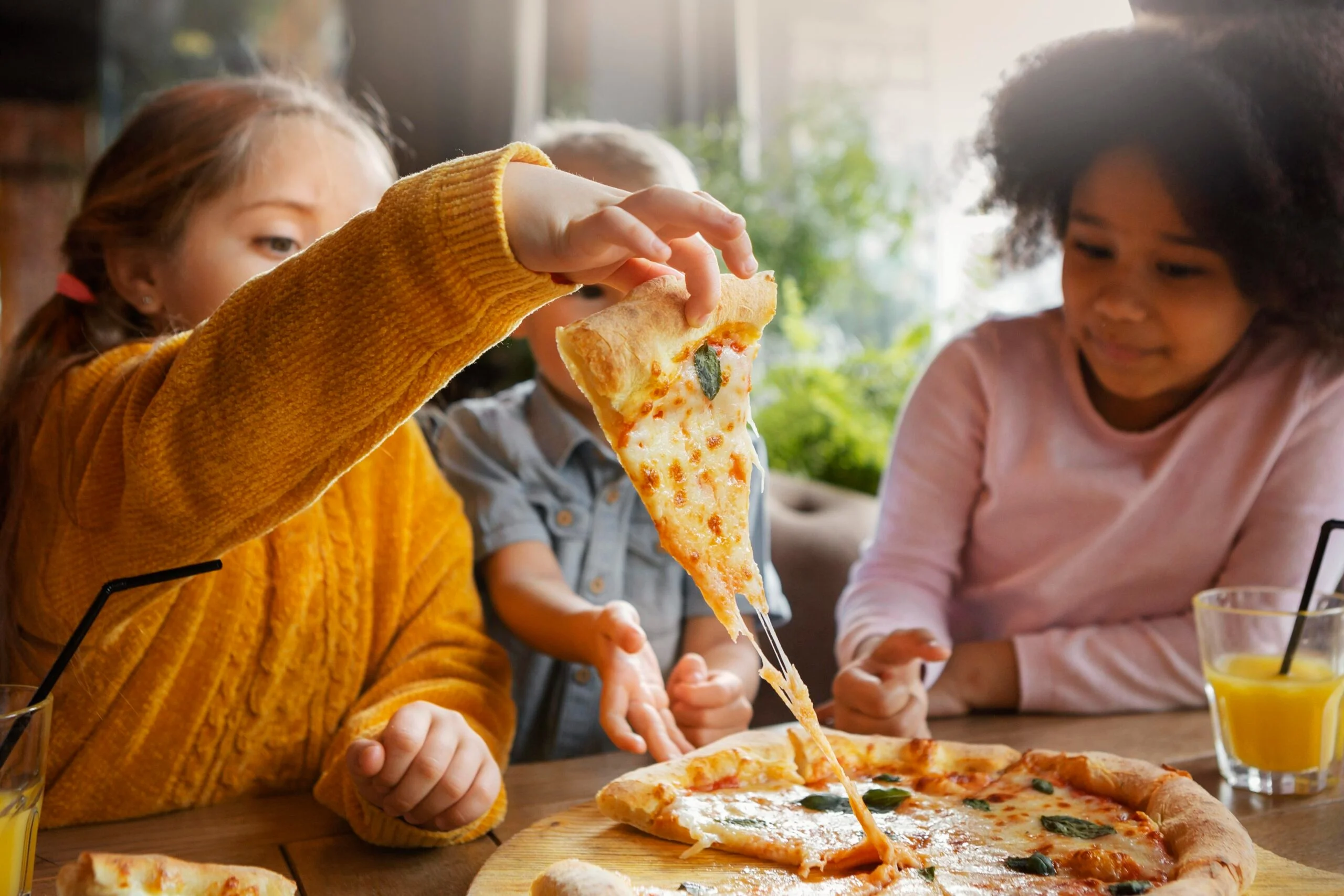 Children enjoying pizza at a restaurant, seated at a table.