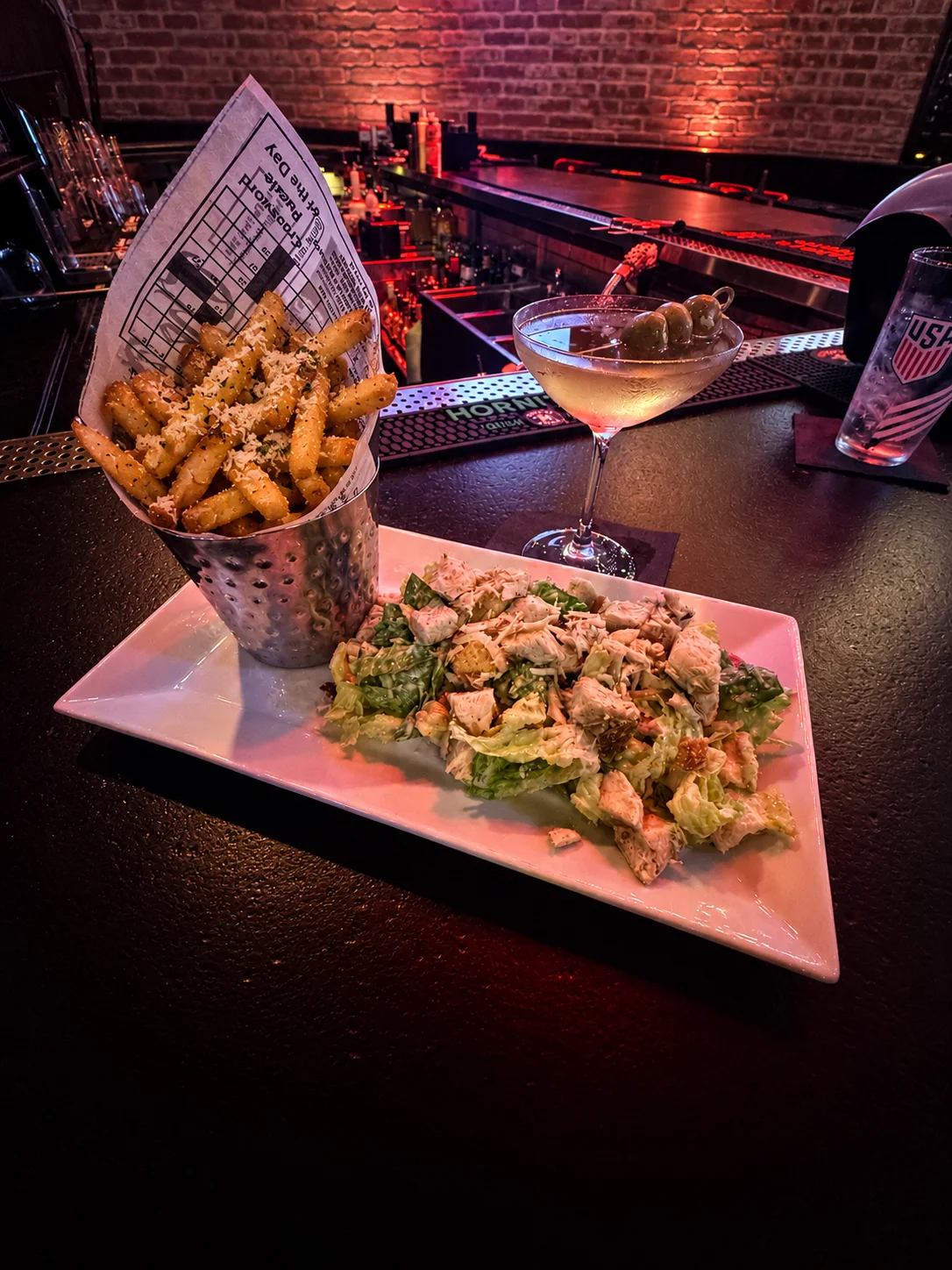 Chicken Caesar salad with seasoned fries and olive-garnished martini at a bar