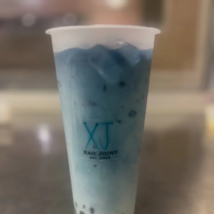 A clear cup filled with a blue and white drink, featuring ice and a branded logo.
