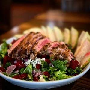 Grilled chicken salad with mixed greens, berries, and sliced apples.