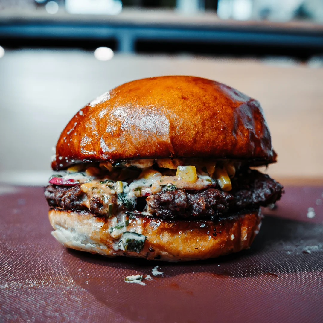 A delicious burger featuring a beef patty and a glossy bun, topped with a creamy sauce.