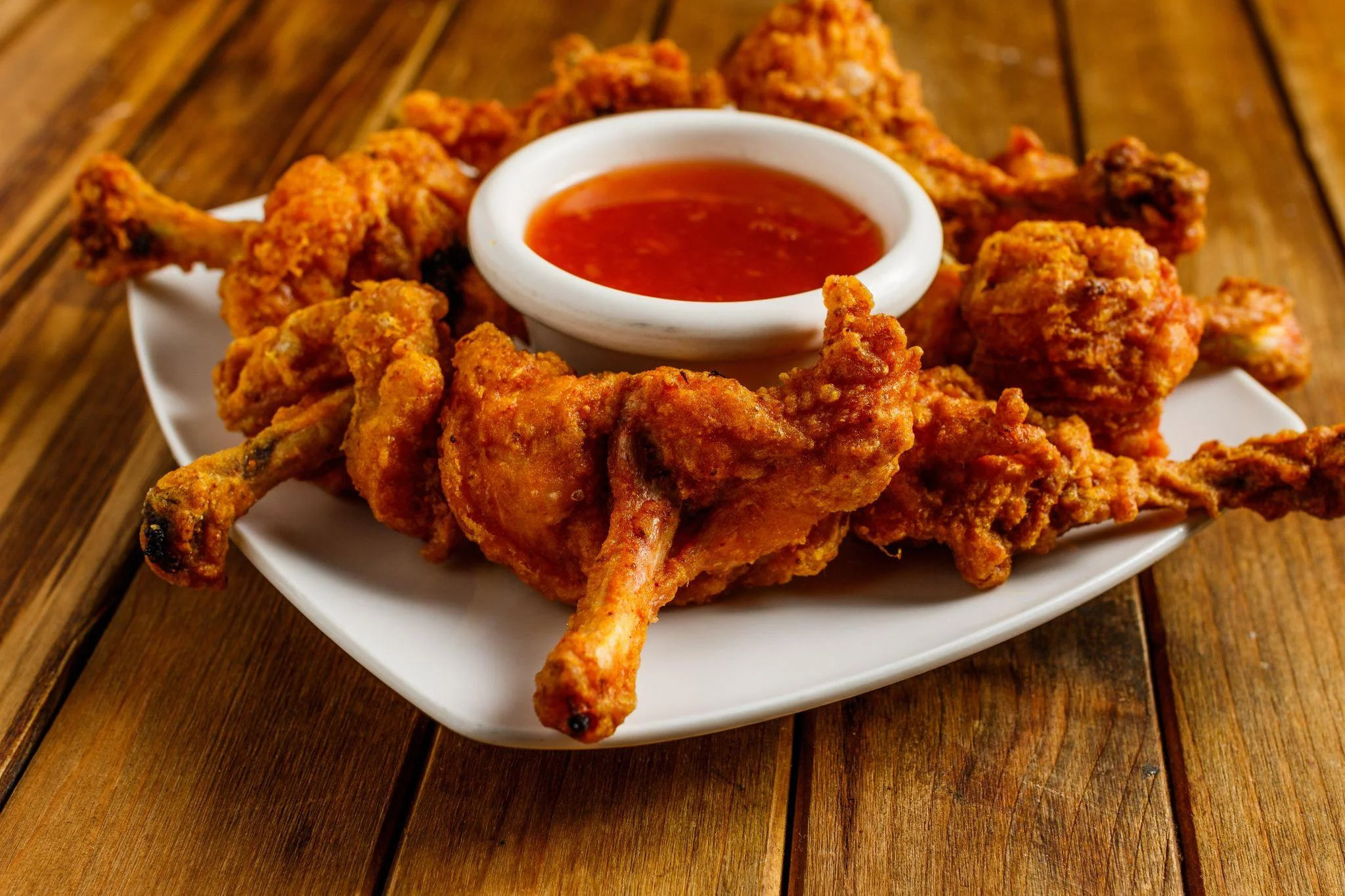 A plate of crispy fried chicken drumsticks arranged around a small bowl of dipping sauce.