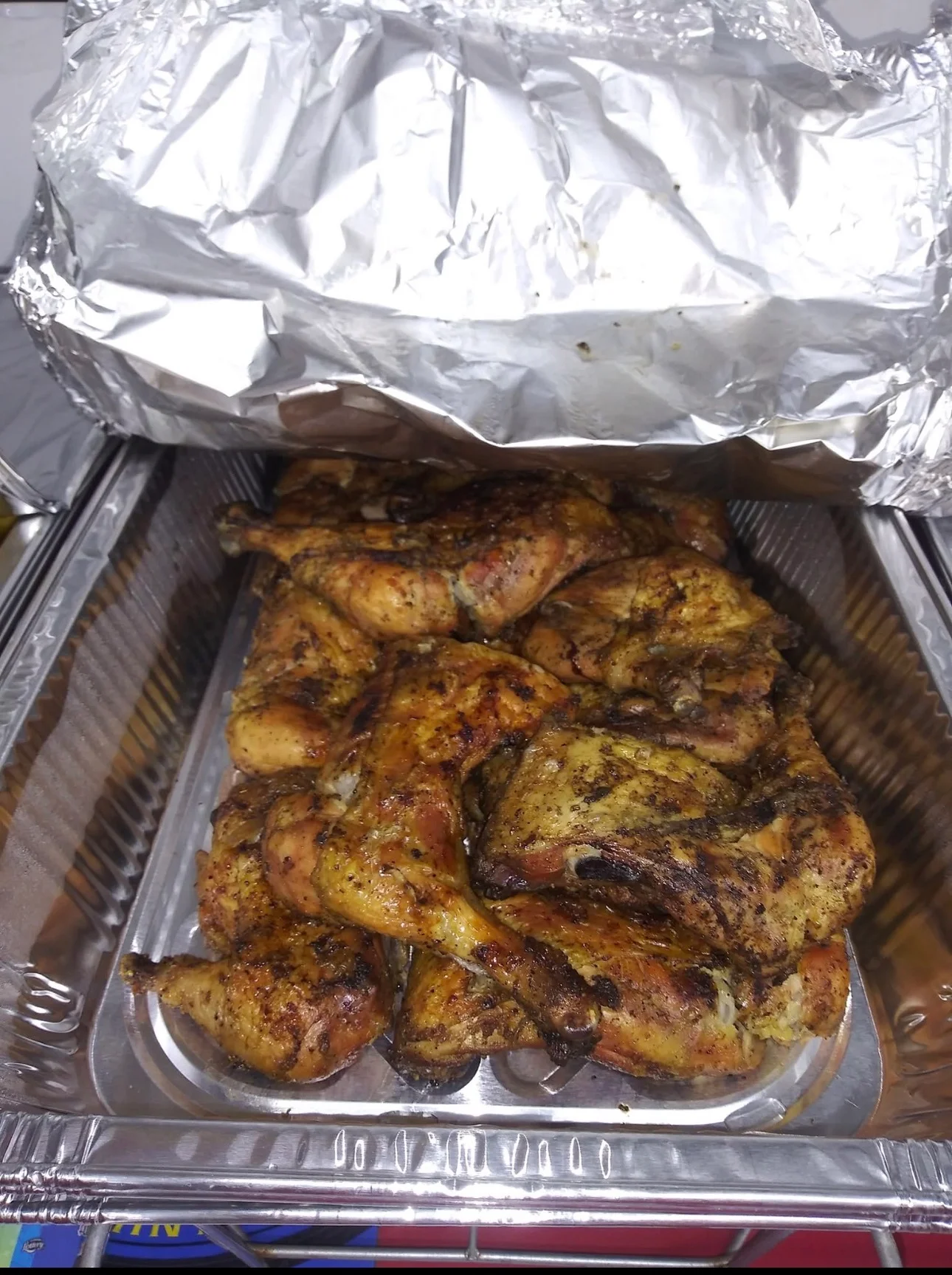 A serving tray filled with seasoned roasted chicken pieces, covered with foil.