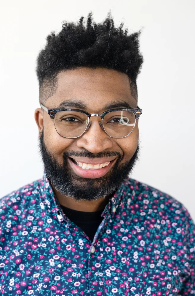 Smiling man with glasses in a floral shirt against a white background