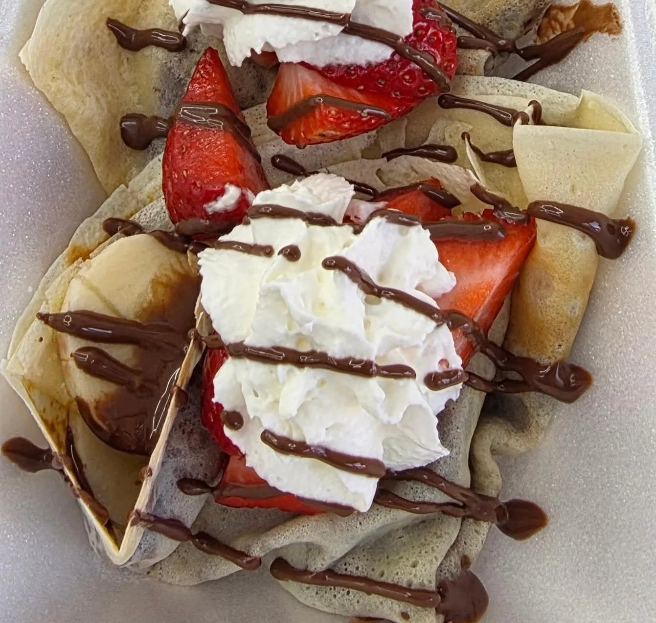A plate of crepes topped with whipped cream and fresh strawberries, drizzled with chocolate sauce.