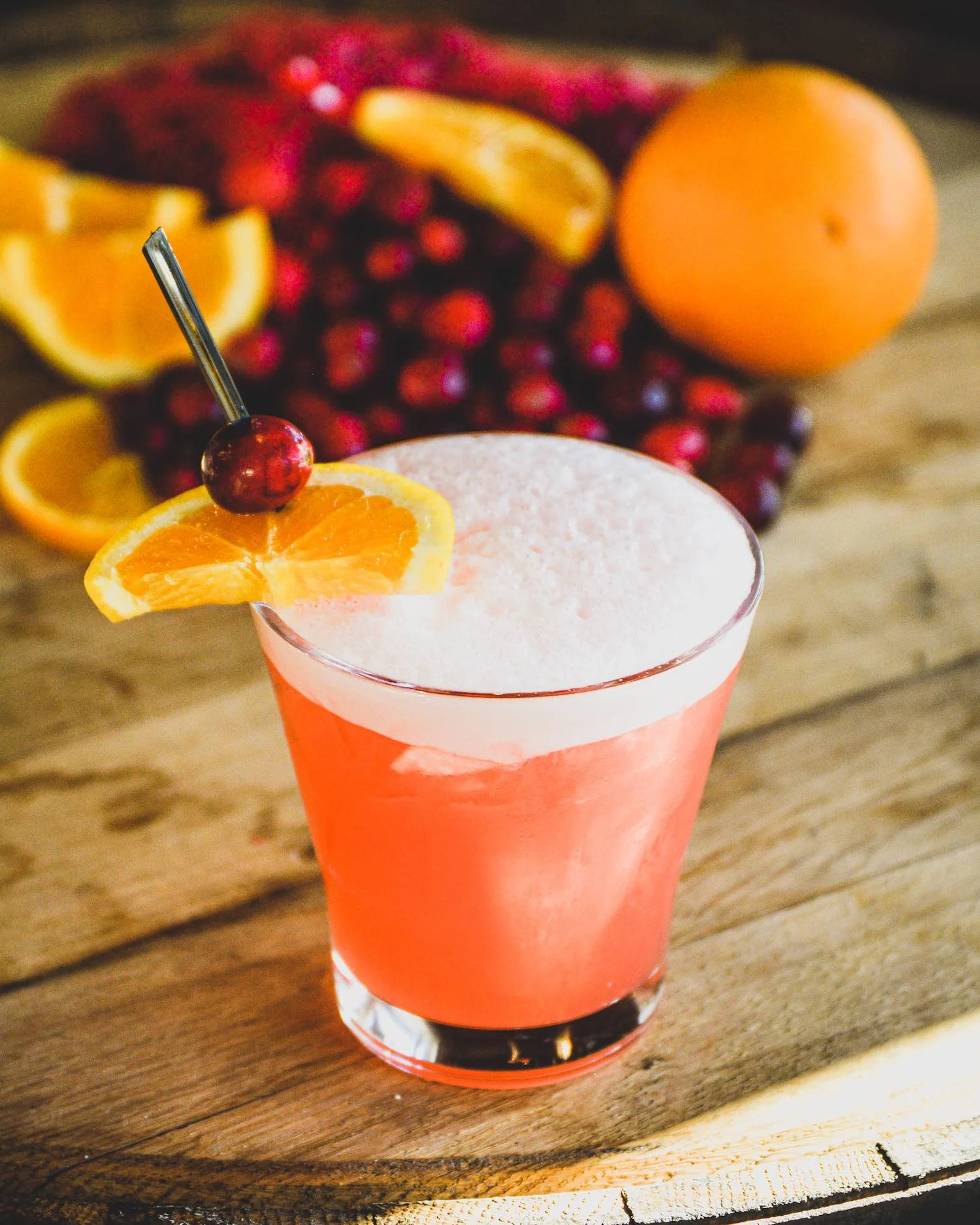 Cran-Orange Sour with orange slices and cranberries surrounding the cocktail